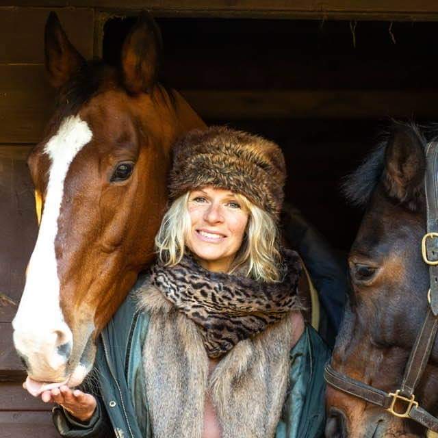 Lisa Hamilton-Smith, life and AI strategist, smiling between two horses at a stable door